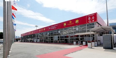 Large exhibition hall tent exterior with flagpoles and red carpet entrance