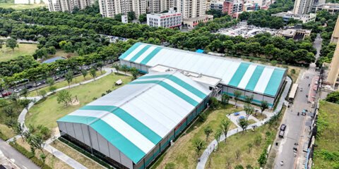 Aerial view of white and turquoise sports tent buildings beside residential towers and landscaped paths