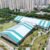 Aerial view of white and turquoise sports tent buildings beside residential towers and landscaped paths