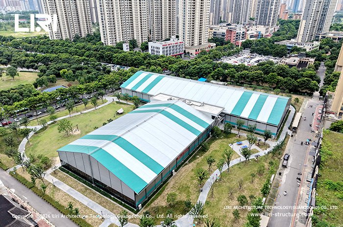Aerial view of white and turquoise sports tent buildings beside residential towers and landscaped paths