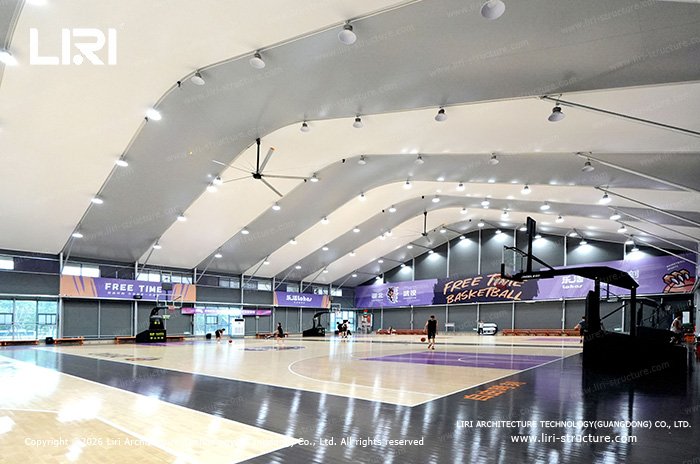 Basketball courts with hoops, lighting and ceiling fans beneath a high fabric roof