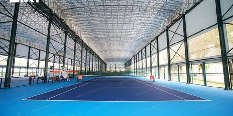 Indoor tennis court with a high truss roof and daylight entering through sidewall panels