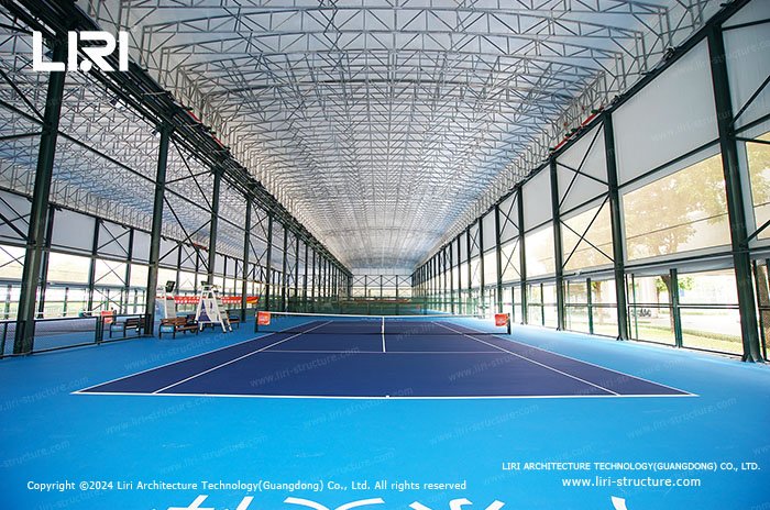 Indoor tennis court with a high truss roof and daylight entering through sidewall panels