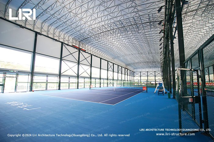 Blue indoor tennis court with translucent upper wall panels and clear lower sidewalls