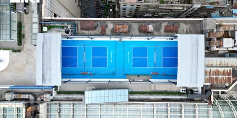 Aerial view of blue pickleball courts with white roof sections retracted at both ends