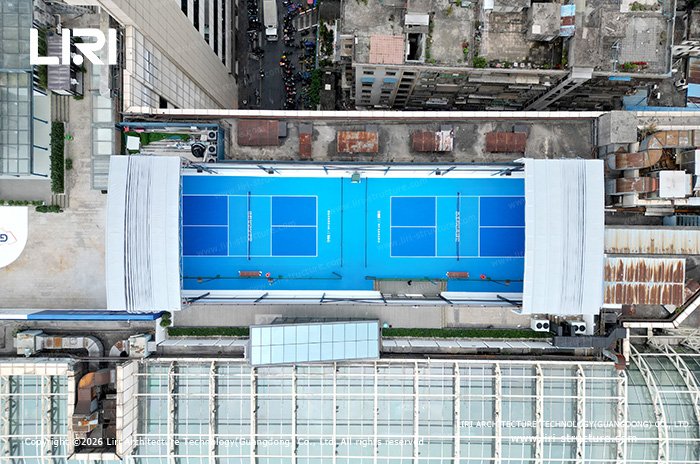 Aerial view of blue pickleball courts with white roof sections retracted at both ends