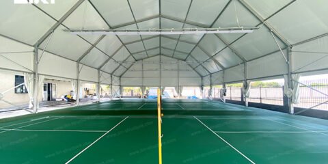 Green badminton courts and nets beneath a white fabric roof with raised side curtains