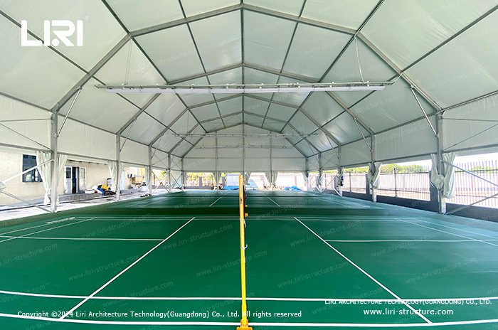 Green badminton courts and nets beneath a white fabric roof with raised side curtains