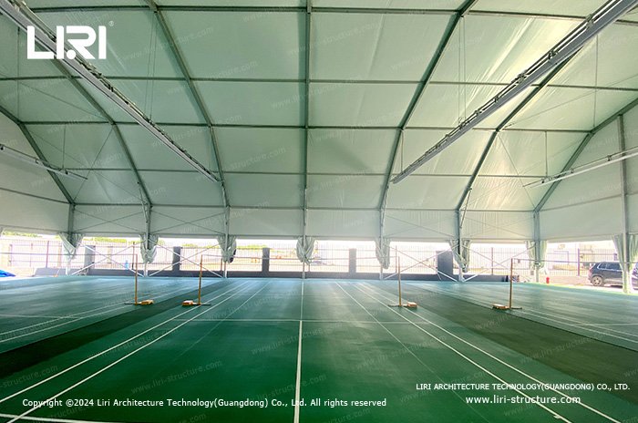Badminton courts beneath a high fabric roof with metal framing and suspended lights